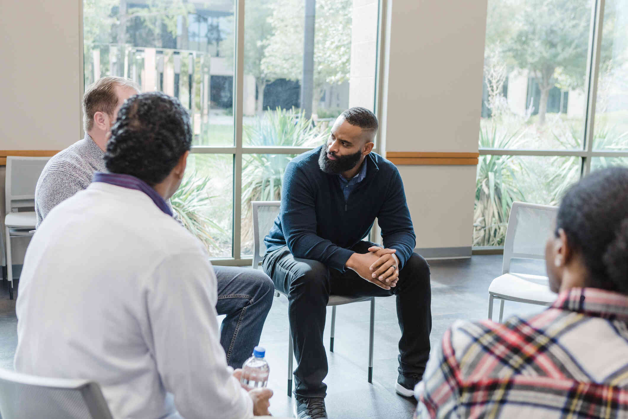 A group of men sit in chairs in a cirlce and talk with serious expressions during a group therapy session.